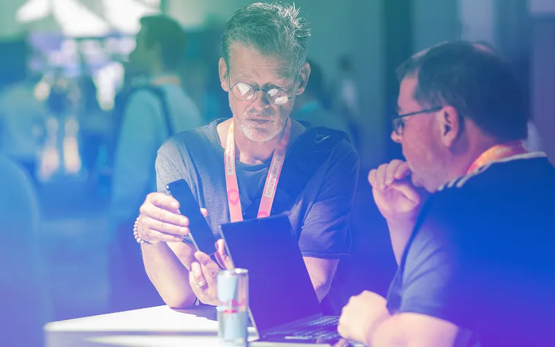 Jamf Nation Live attendee compares iPhone and laptop screens while discussing Apple management with a colleague.