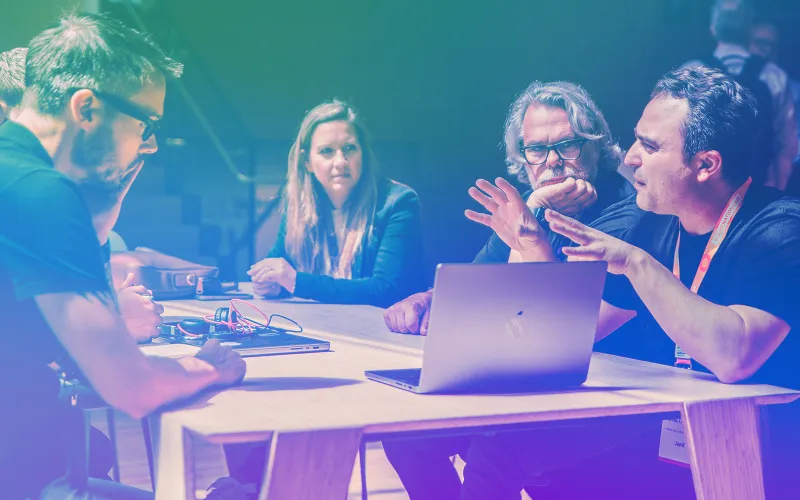 Four IT professionals with a MacBook discuss Apple device management strategy at a Jamf conference table.