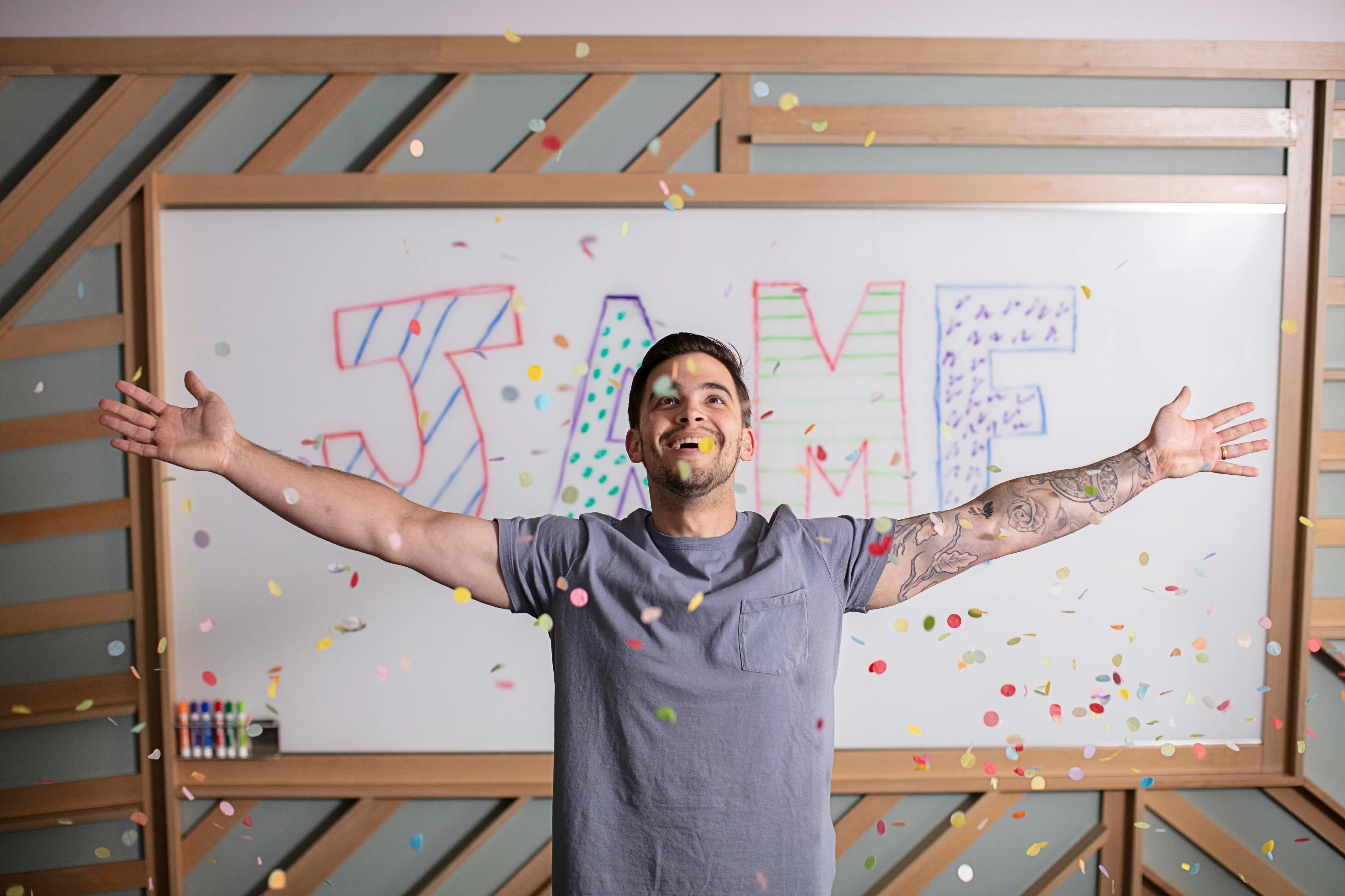 A man with outstretched arms smiles as colorful confetti falls around them, with the word