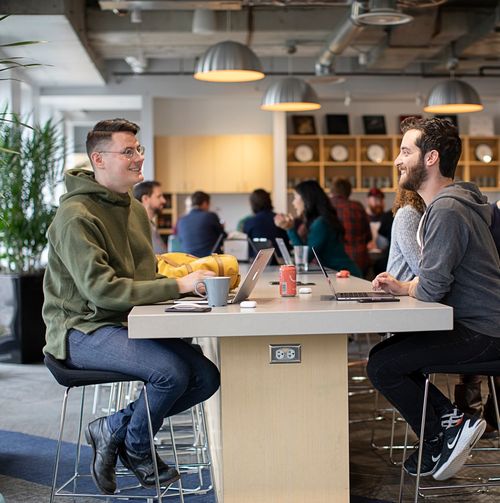 A pair of Jamf employees smiling and collaborating with Apple macBooks in a modern office space.