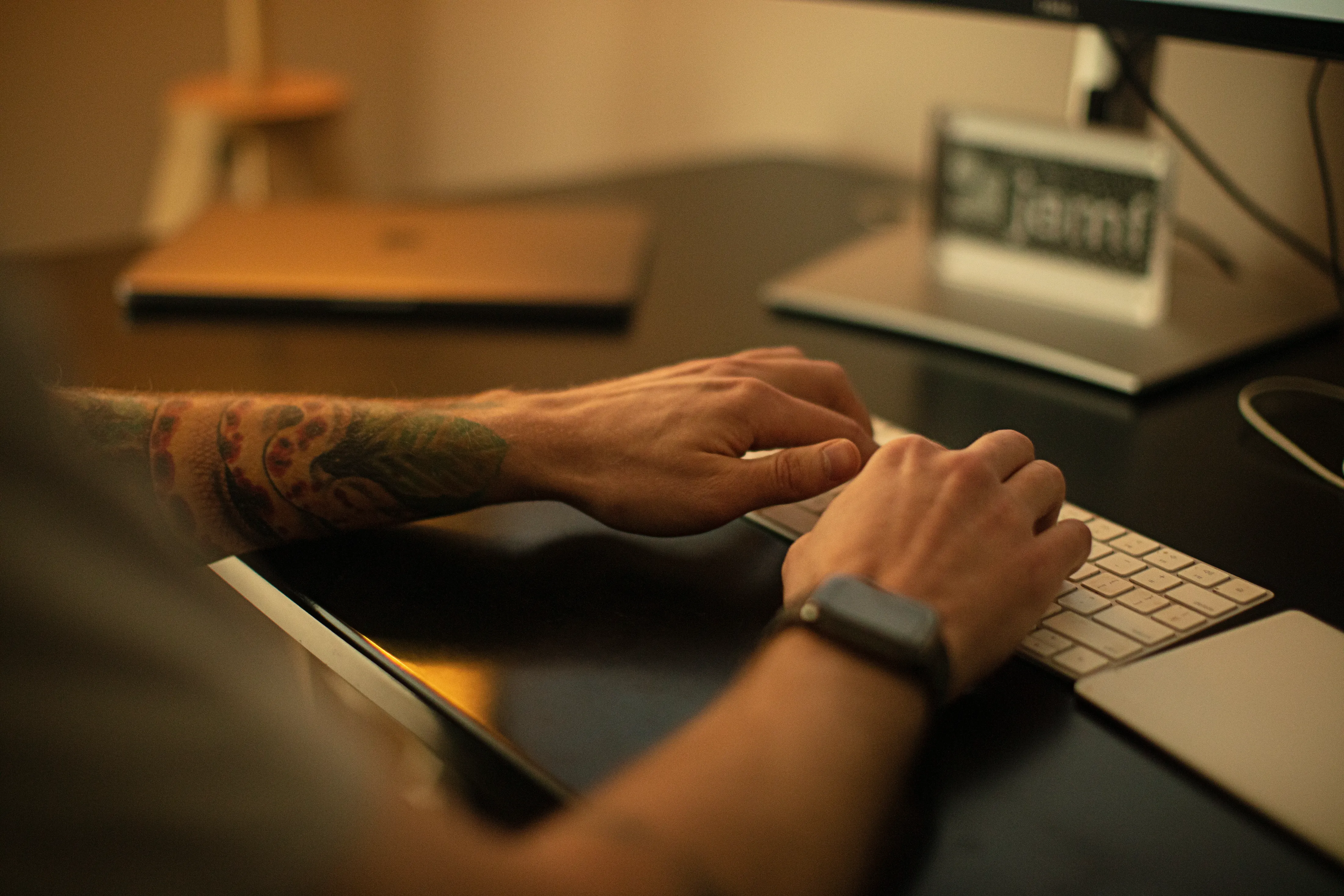 A Jamf employee with a tattoo on his forearm types on his Apple keyboard.