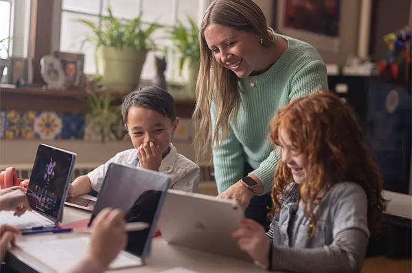 Teacher showing two students how to work on their iPads.