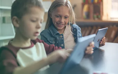 Two kids helping each other on iPads in their classroom.