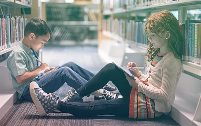 Two kids using iPads in the library.