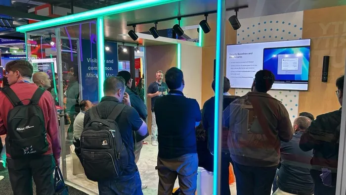 A Jamf employee presenting about security benchmarks at their RSAC booth as conference attendees look on