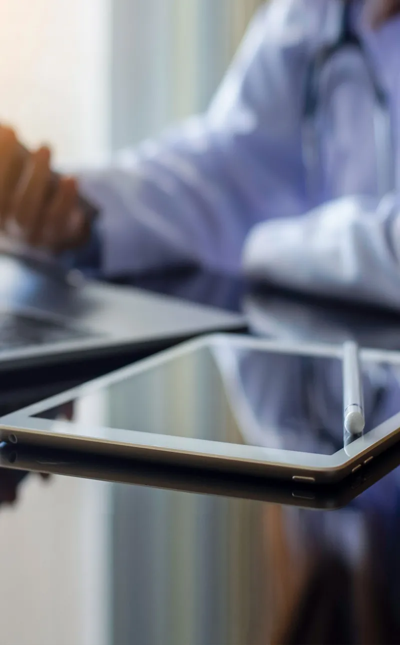 Doctor checking iPhone while using a MacBook and iPad.