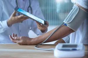 Doctor using an iPad to record a patient's blood pressure reading during a clinical exam.