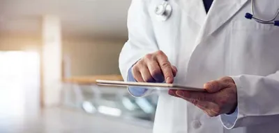 Doctor in white coat with stethoscope using an iPad tablet in a hospital corridor.