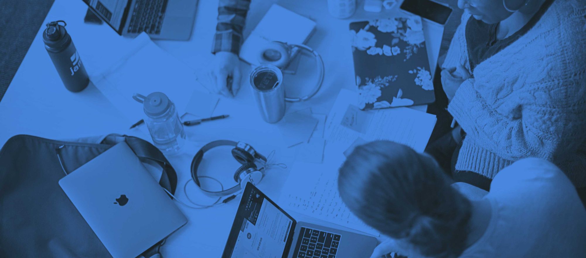 People working at a desk with Apple products, shot from overhead