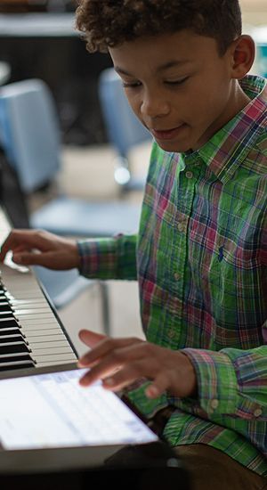 Student plays a piano and uses an iPad managed by Jamf during music lesson.