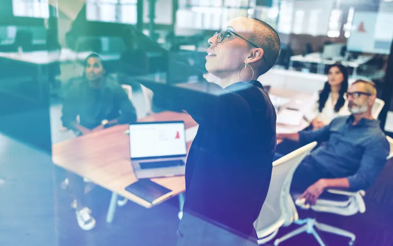 A diverse agile development team works on a glass whiteboard during a collaborative planning session in a modern tech office.