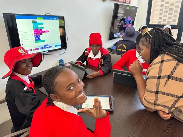Children in red uniforms learn to code with a teacher.