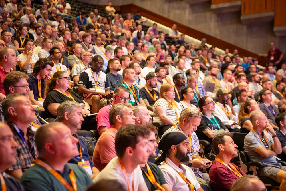 A large, diverse audience sits in a tiered auditorium, attentively watching a presentation during the Jamf Nation Live London event.