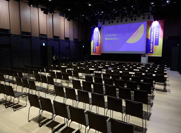 Empty main hall at Jamf Nation Live Tokyo 2025 with rows of chairs facing a branded stage and networking slide on screen