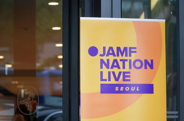 A close-up shot of a Jamf Nation Live promotional banner displayed near a building entrance in Seoul. The banner features a gradient background from yellow to orange with the