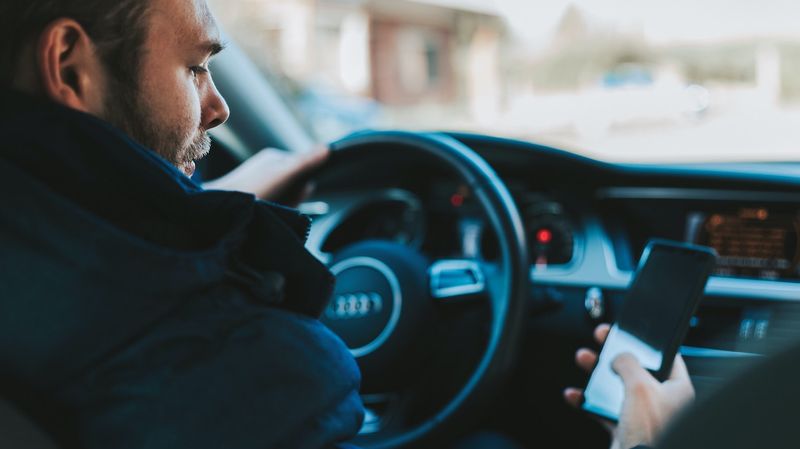 A man looking at his smart phone while behind the wheel of a car