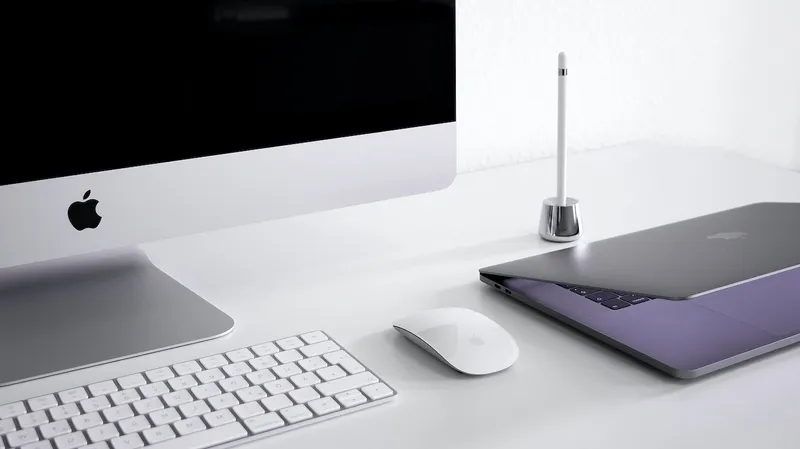 A MacBook sitting on a desk beside a wireless mouse, keyboard, monitor and pen holder