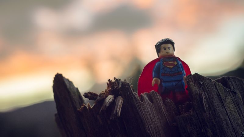 A Superman figure standing atop a tangled piece of wood, with an out-of-focus sunset in the background