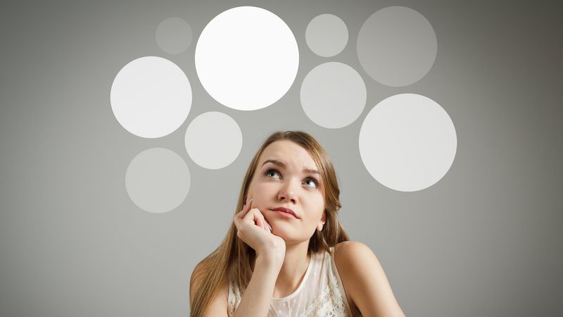 A woman looking up with a thoughtful expression with abstract white circles floating above her head