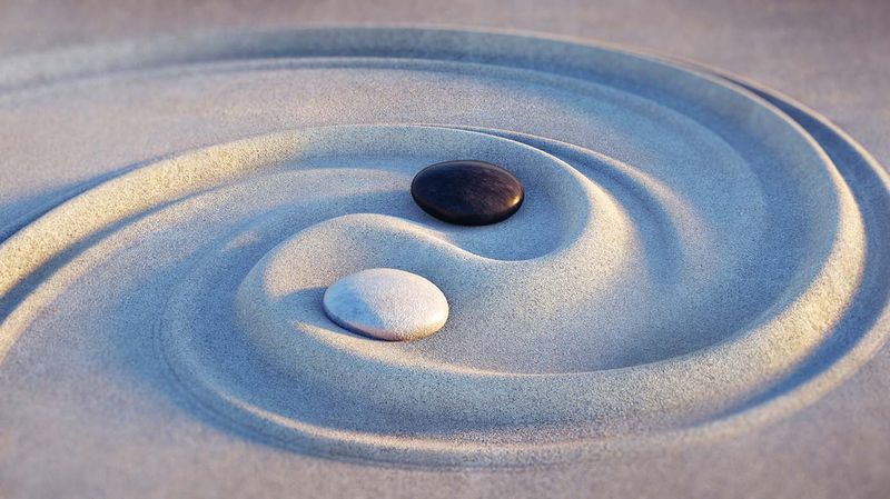 Zen sand art in a circular pattern with one white and black stone intimating yin & yang