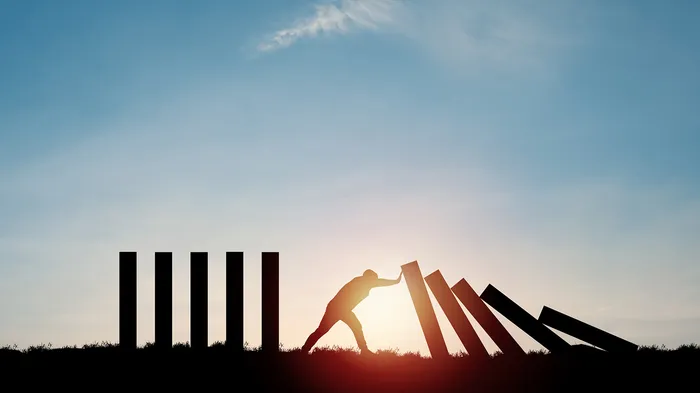 The silhouette of a person holding back blocks from falling over, like a domino effect.