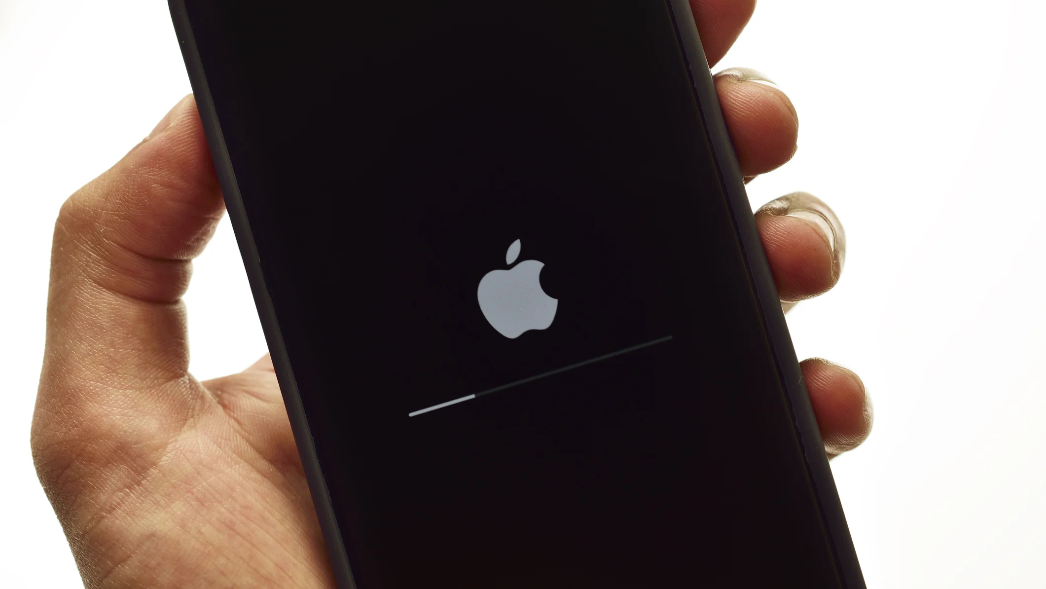 A hand holds up an iPhone which is restarting to enable iOS 18.
