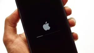 A hand holds up an iPhone which is restarting to enable iOS 18.