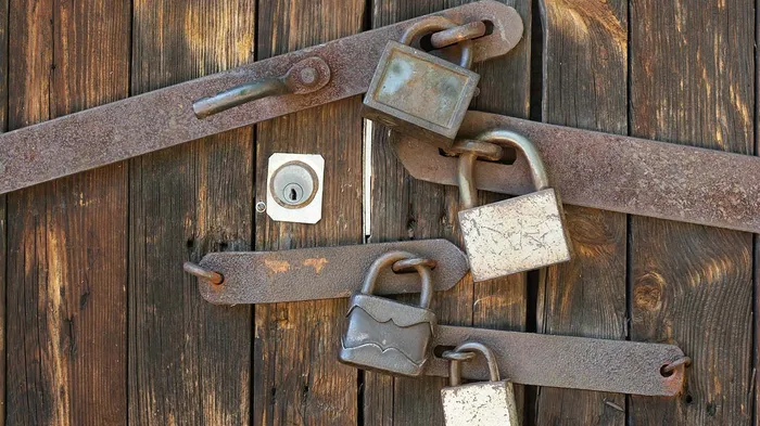 Wooden door secured with deadbolt and multiple padlocks and reinforcement bars.