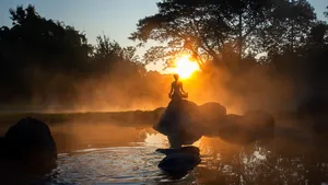 Woman mediating atop a rock overlooking a lake at sunset.