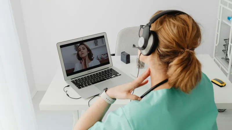 A clinician conducts a virtual telehealth session with a hospitalized patient using an iPad and Macbook, both managed by Jamf.