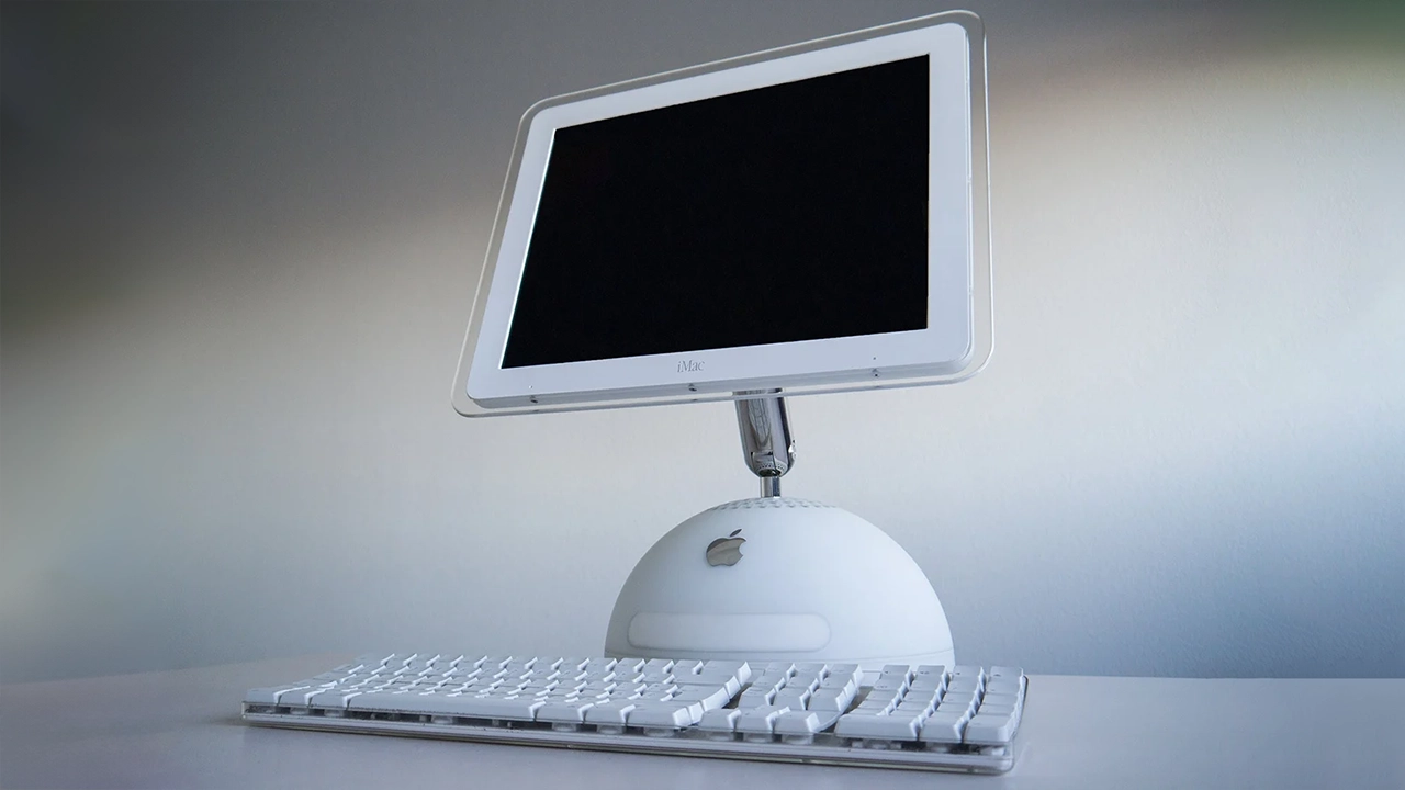 An iMac G4: an Apple keyboard in front of a screen with a lamp-like design.