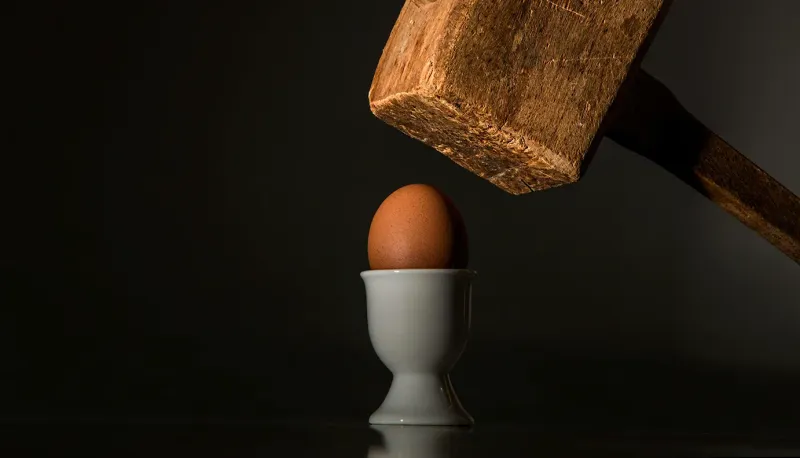 A vulnerable egg is about to get smashed by a large wooden hammer.