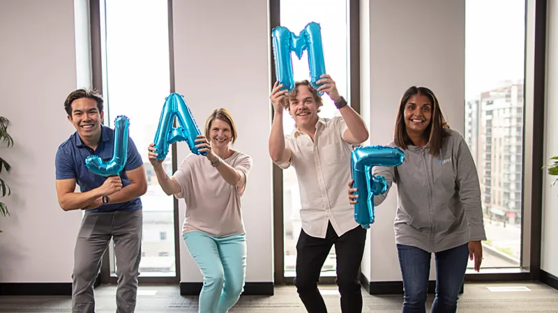 Four Jamf employees hold up blue metallic balloons that spell out: Jamf.