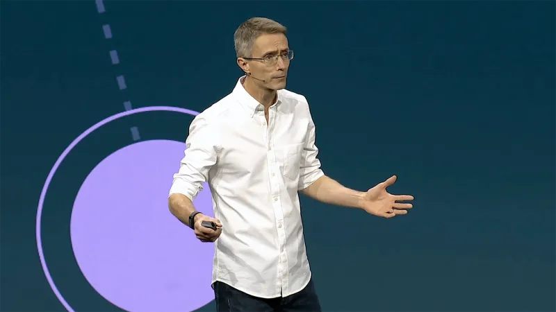 Mike Campin stands in front of a JNUC 2025 background, gesturing as he speaks. He has short-cropped salt-and-pepper hair and wears a white dress shirt rolled up at the sleeves.
