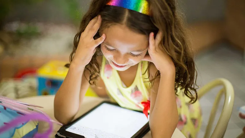 A grade-schooler sits at a low table in a classroom, propping her head up in her hands. She has long brown hair and consults an iPad managed by Jamf School.