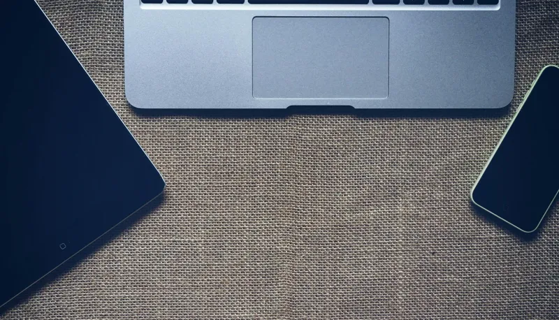 A MacBook, iPad, and iPhone on top of an empty desk.