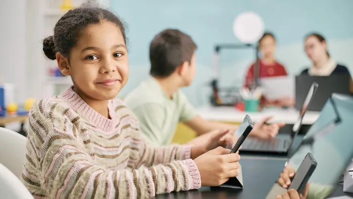 Young student with a soft smile in a classroom holding an iPad and looking at the camera