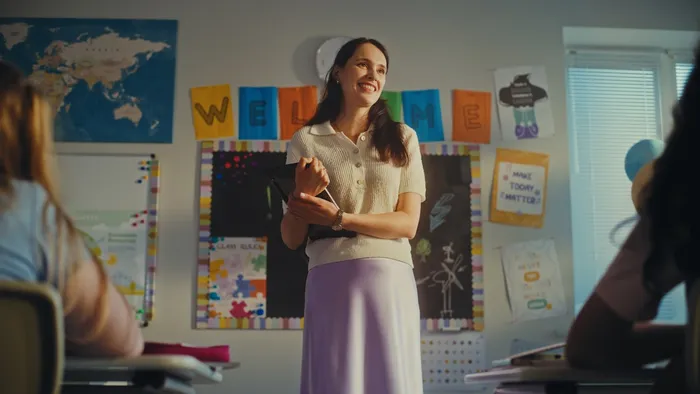 Smiling teacher in front of classroom holding an iPad
