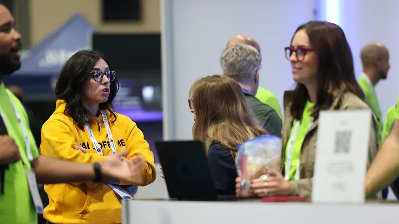 Support team members assist visitors to their booth at the 2026 JNUC. Those foregrounded wear bright colors and talk animatedly.