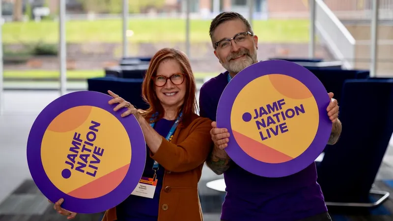 Two people smiling and holding up circular Jamf Nation Live signs