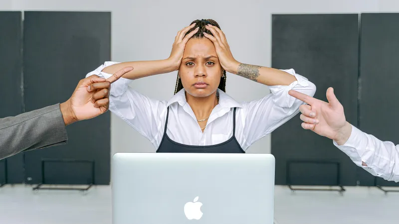 An IT staff member clutches her head in frustration as two arms reach in from either side to point fingers.