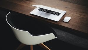 Wooden desk with a MacBook and Magic Mouse on top. White chair in front of the desk.
