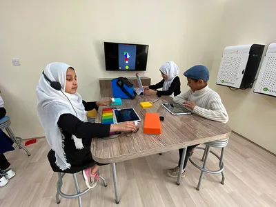 MATTER Innovation Hub students at work in Afghanistan. A girl in a black dress, sneakers, and a white headscarf crowned by headphones works with Sphero Specdrums and a Musical Play Pad. Across a table another girl in a black dress and white headscarf