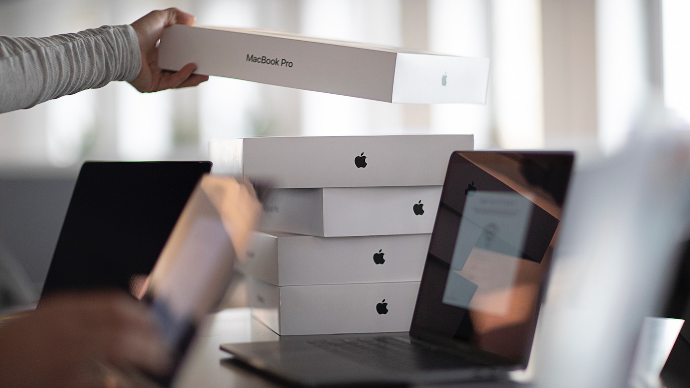 Boxes of MacBook Pros are stacked on a desktop awaiting enrollment into MDM with Jamf.