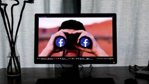 computer monitor shows man looking through binoculars with Facebook logos in the lenses.