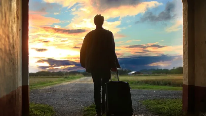Person walking into the sunset with a rolling suitcase.