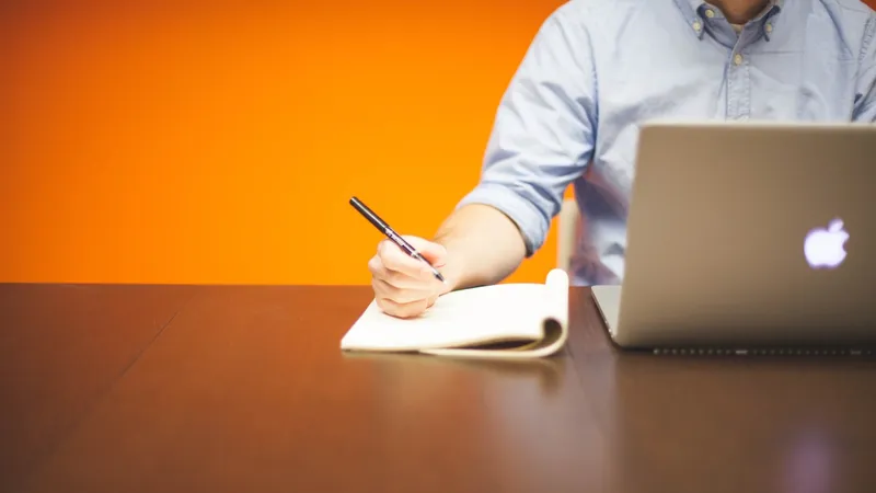 Person writing in a note book next to a Mac running Jamf Pro