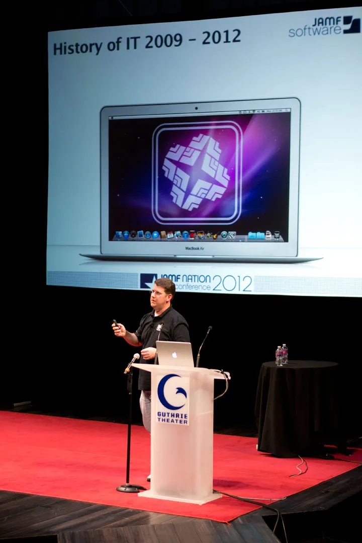 Bryson Tyrrell stands at a podium during jNUC 2012 to explain all the tricks and tips Jamf Pro has to offer for Mac device management.
