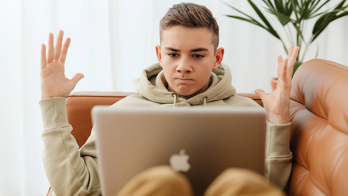 A high school student on a MacBook throwing his arms up in angry frustration when he meets Jamf Safe Internet's On-Device-Content-Filtering.