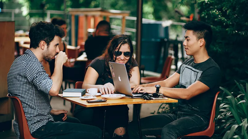 Three startup employees at a cafe table, hard at work on a MacBook managed by Jamf.